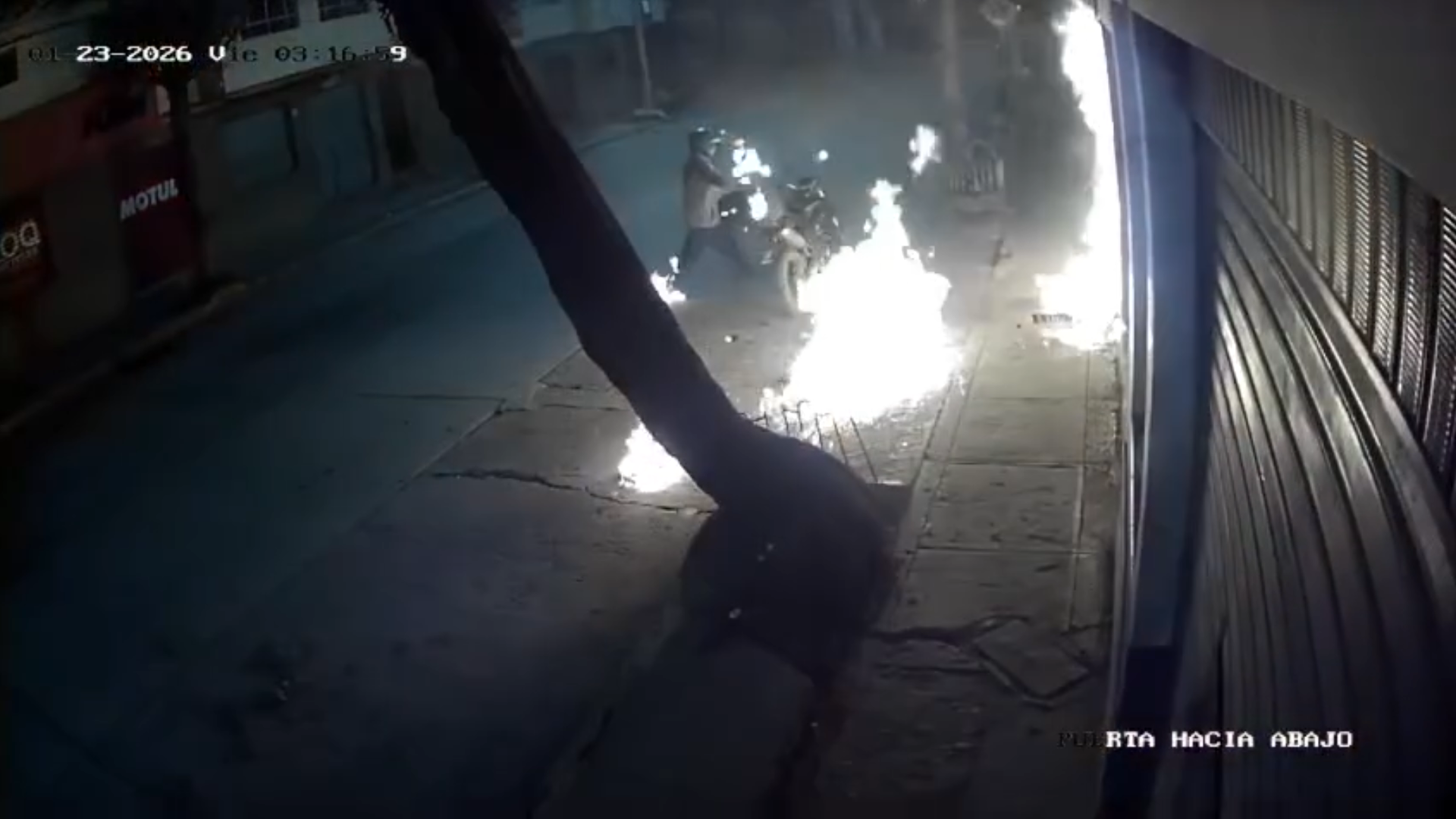 A clear frame from the CCTV video showing flames at the entrance of the motorcycle shop with the suspect nearby, avoiding graphic details.