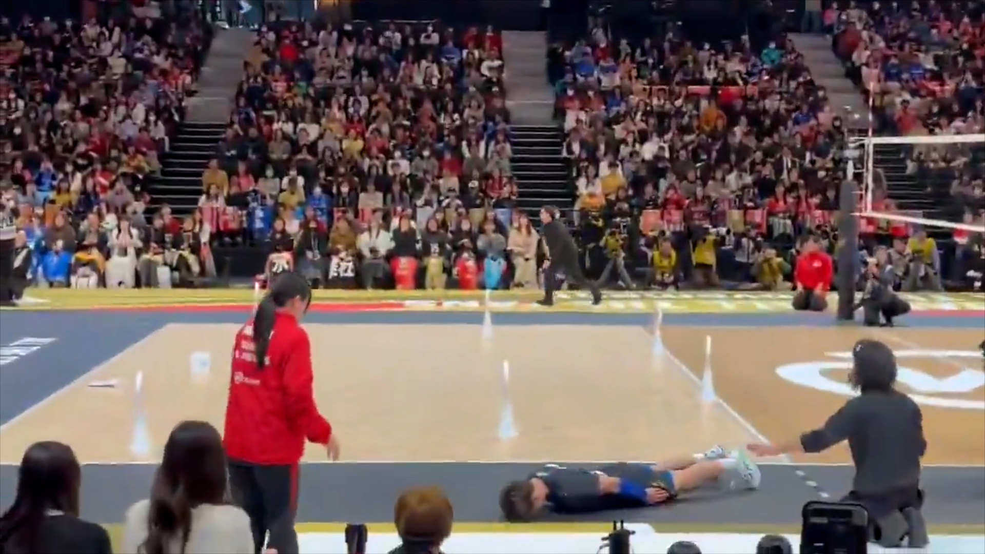 A wide frame from the video showing the player bowing on the court in front of the woman.