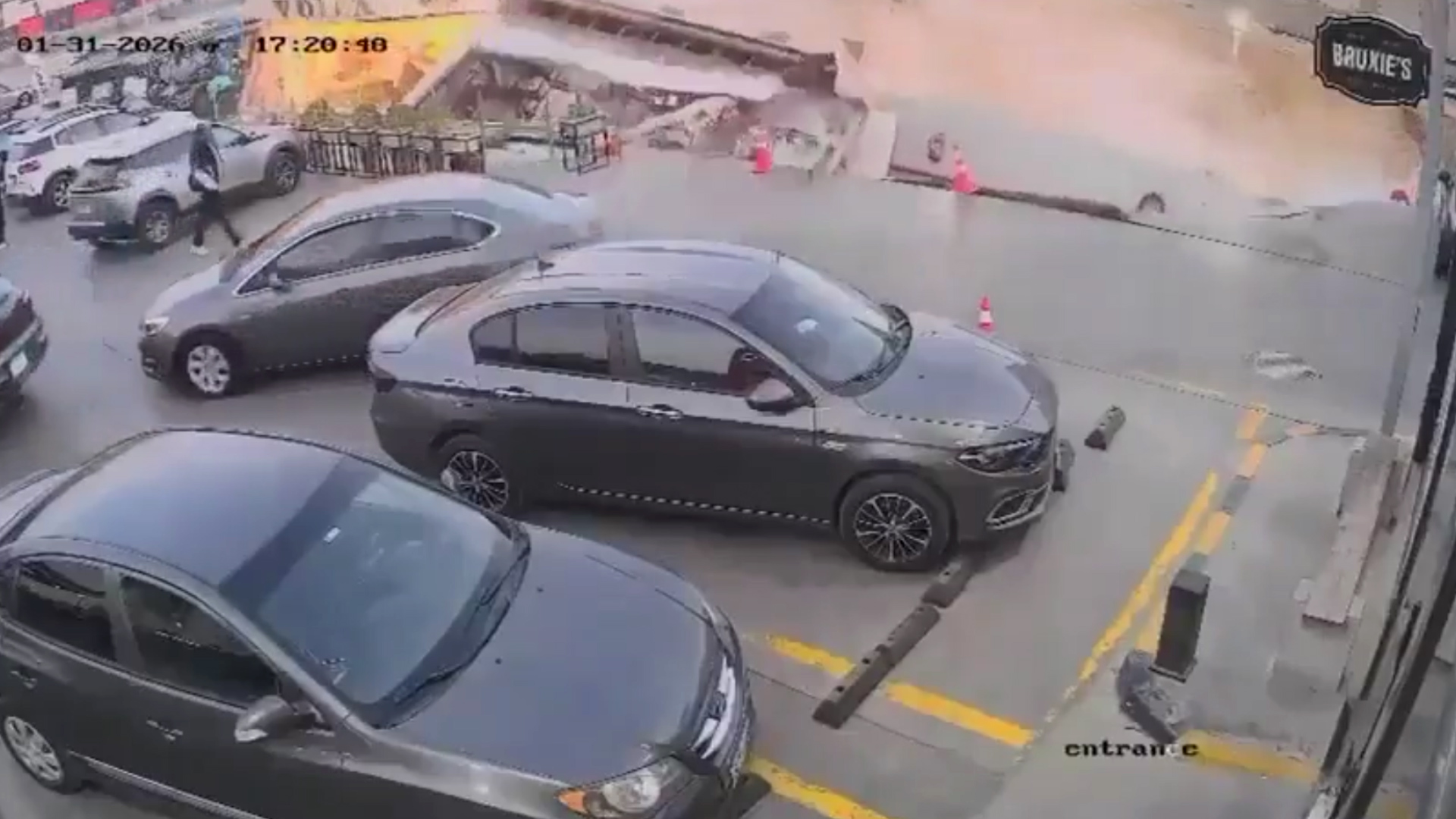 A wide CCTV frame showing the sinkhole forming inside the gas station area.