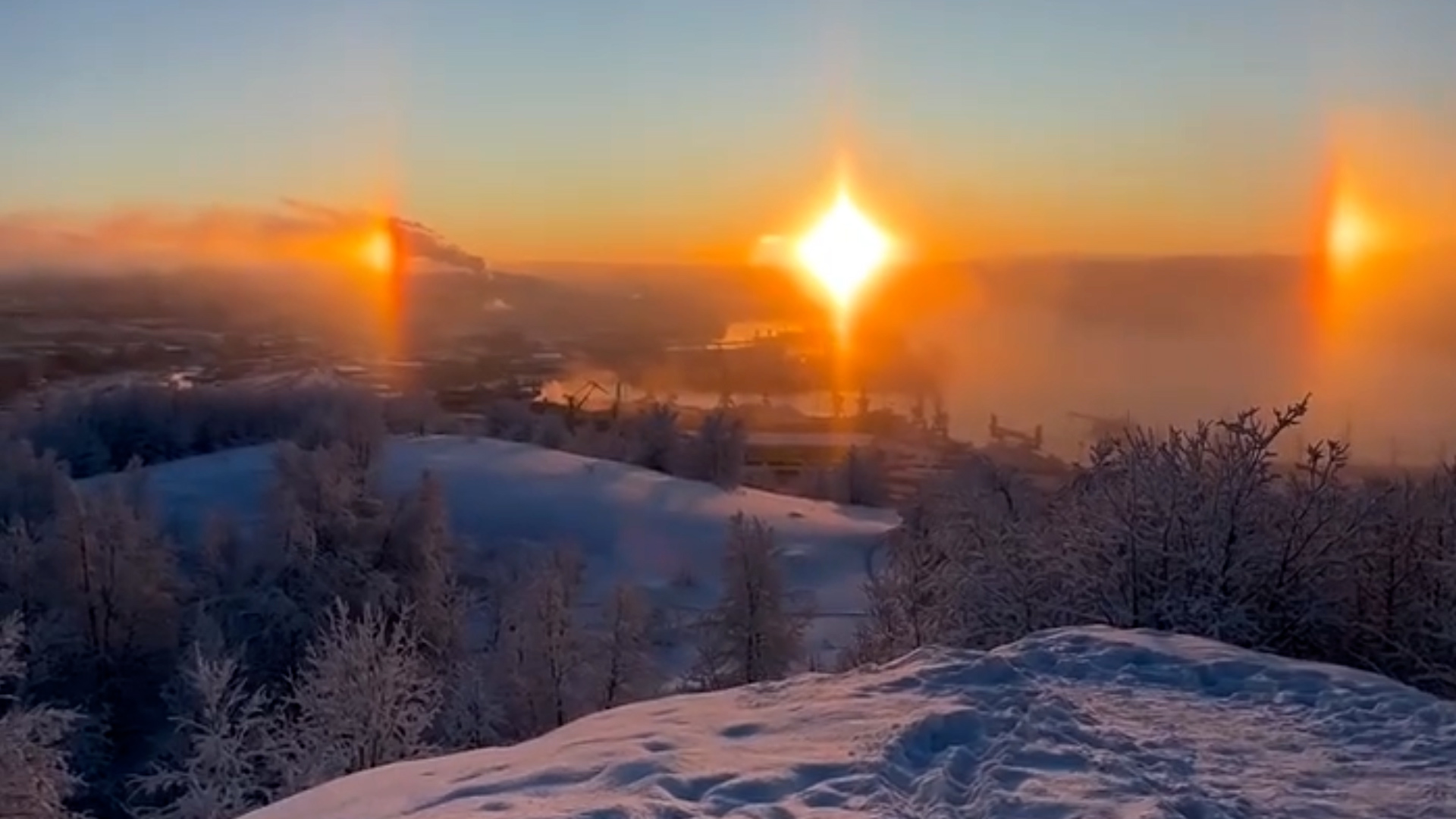 A wide sunset frame showing the central sun with two bright light spots on either side in the Murmansk sky