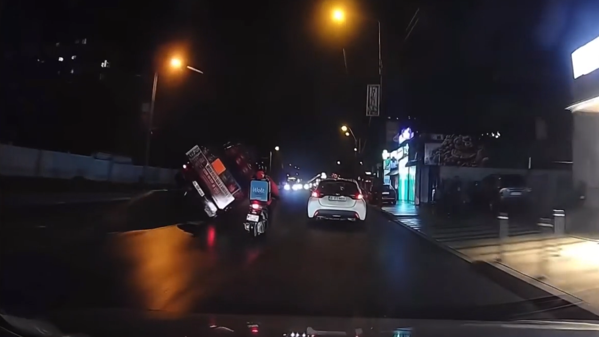 A wide dashcam frame showing the truck beginning to skid on the wet roadway under streetlights, avoiding close-ups of debris or people.